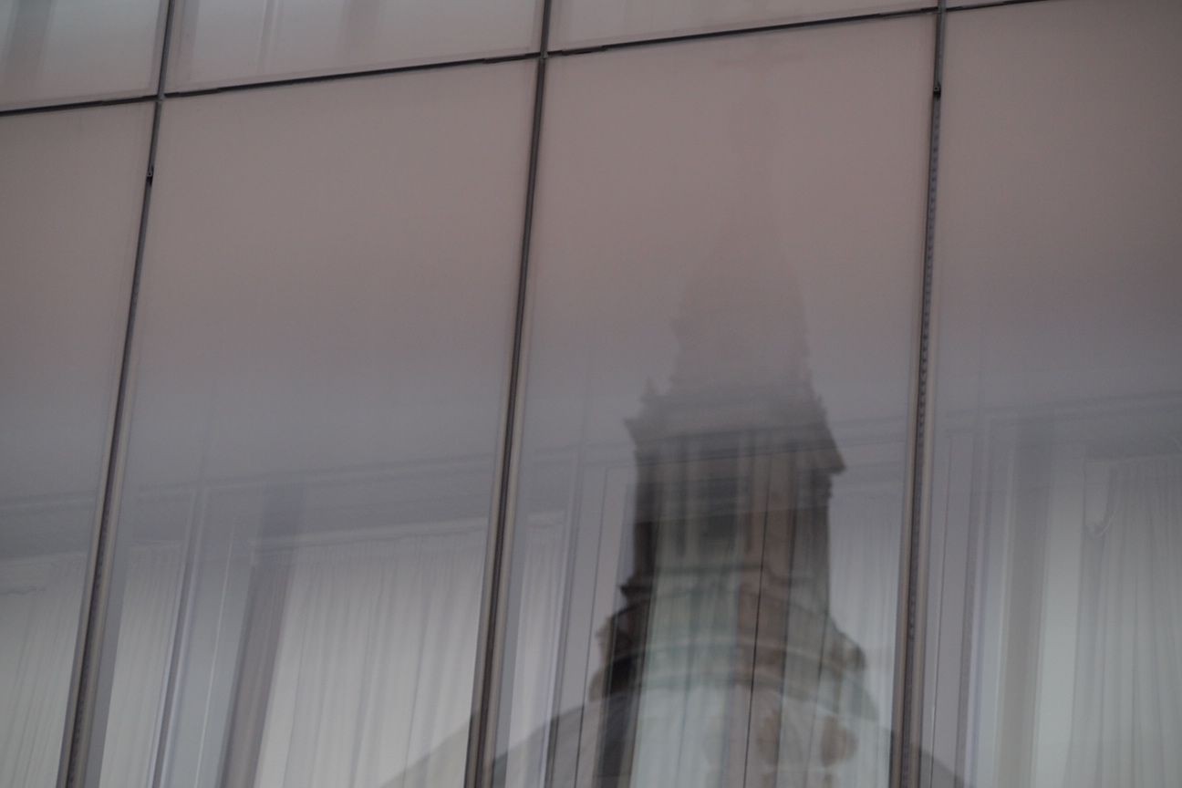 Reflection of a building's tower on a glass facade with minimalistic panels.